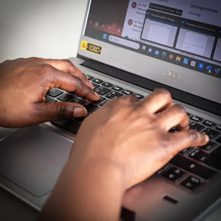 Zwei Hände schreiben an einem aufgeklappten Laptop