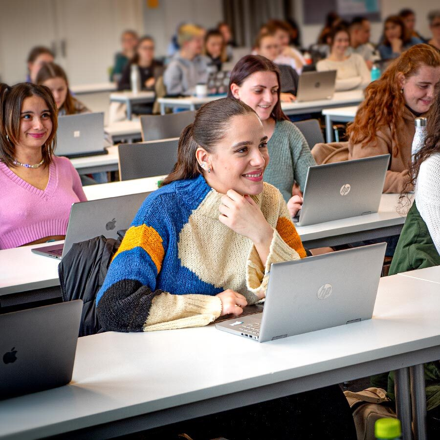 Studentinnen sitzen in Reihen im Hörsaal vor dem Laptop