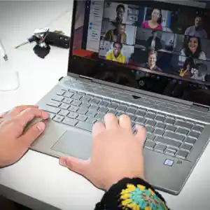Hände am Laptop. Am Laptop ist eine Teamssitzung ersichtlich